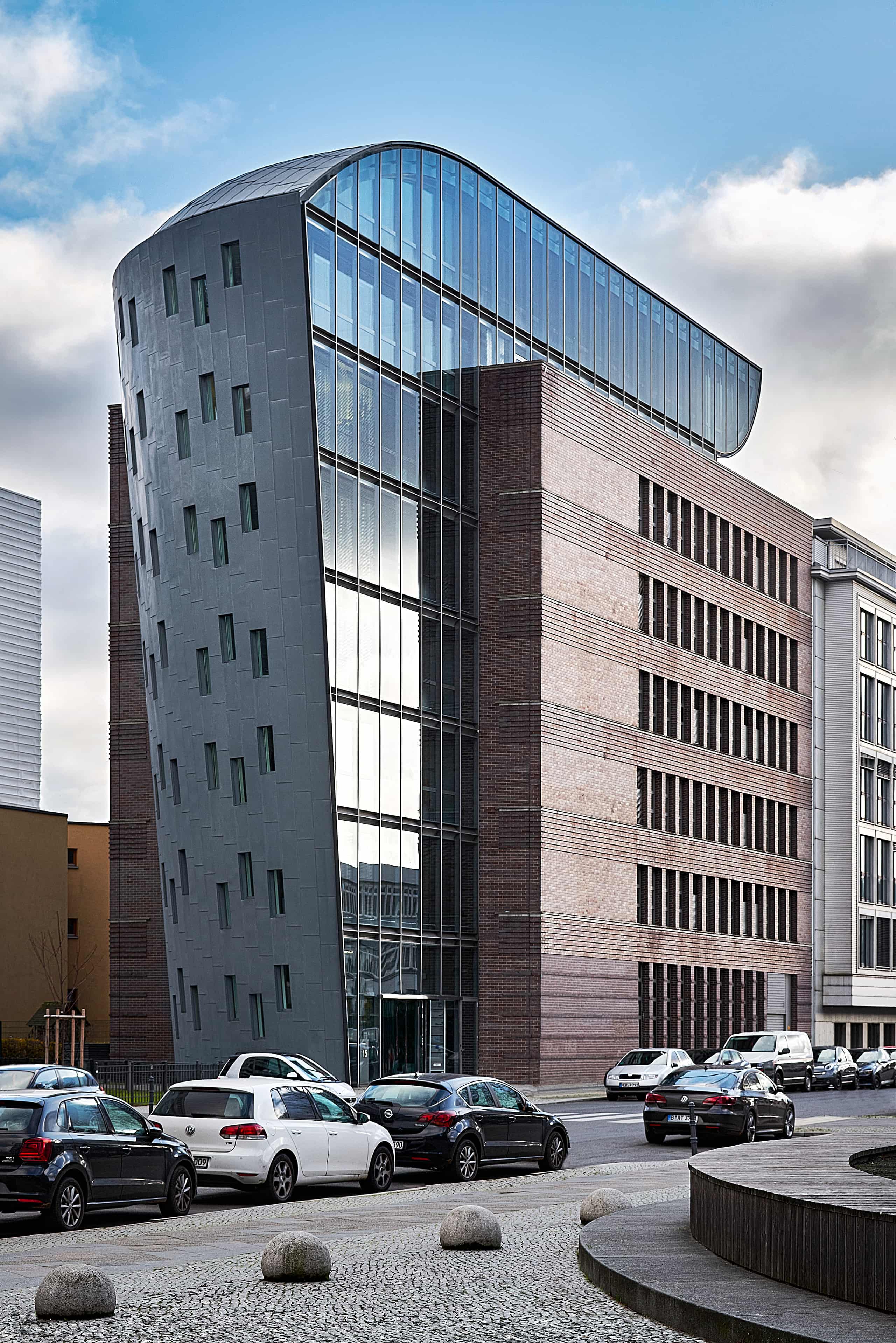 Haus der Presse Berlin, Architekturfotografie für den BDZV: Ein modernes Gebäude mit geschwungener Glasfassade und Ziegelmauerwerk steht an einer Straße mit parkenden Autos