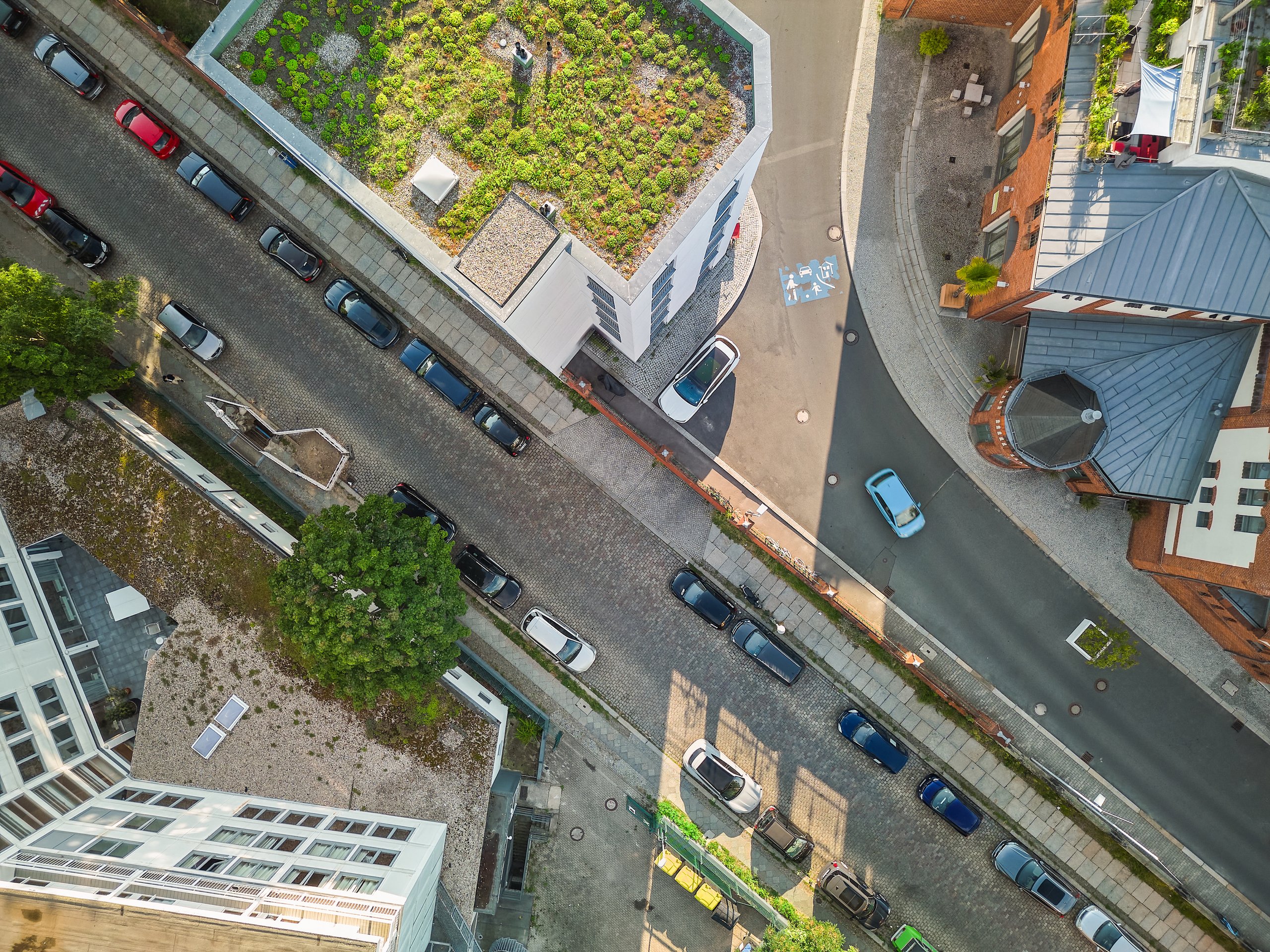 Luftaufnahme von Gebäuden mit begrünten Dächern, gepflasterten Straßen und parkenden Autos in Potsdam.