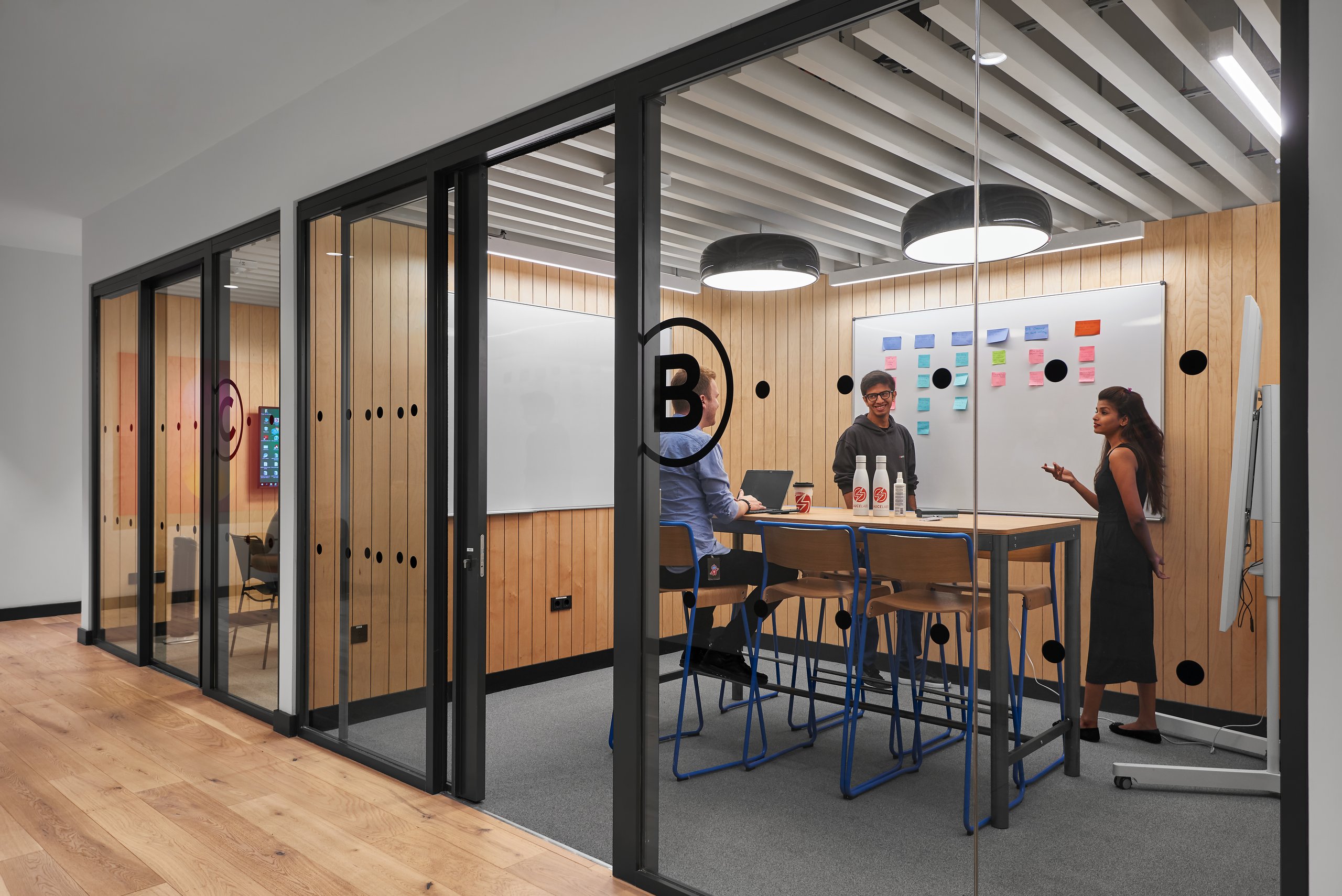 SauceLabs Berlin: Drei Personen in einem modernen Konferenzraum mit Holzwänden, Whiteboards und einem Tisch mit Stühlen
