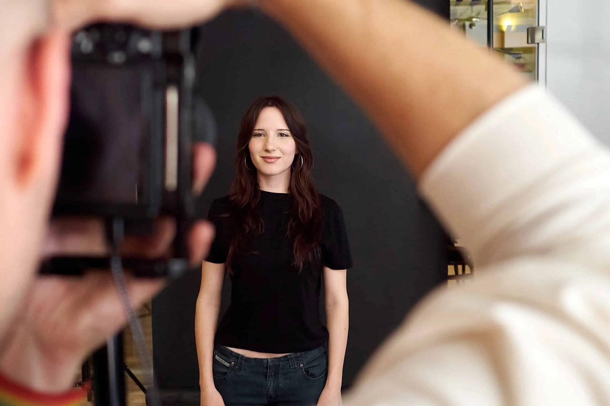 Eine junge Frau mit langen braunen Haaren und schwarzem T-Shirt wird von einem Fotografen fotografiert